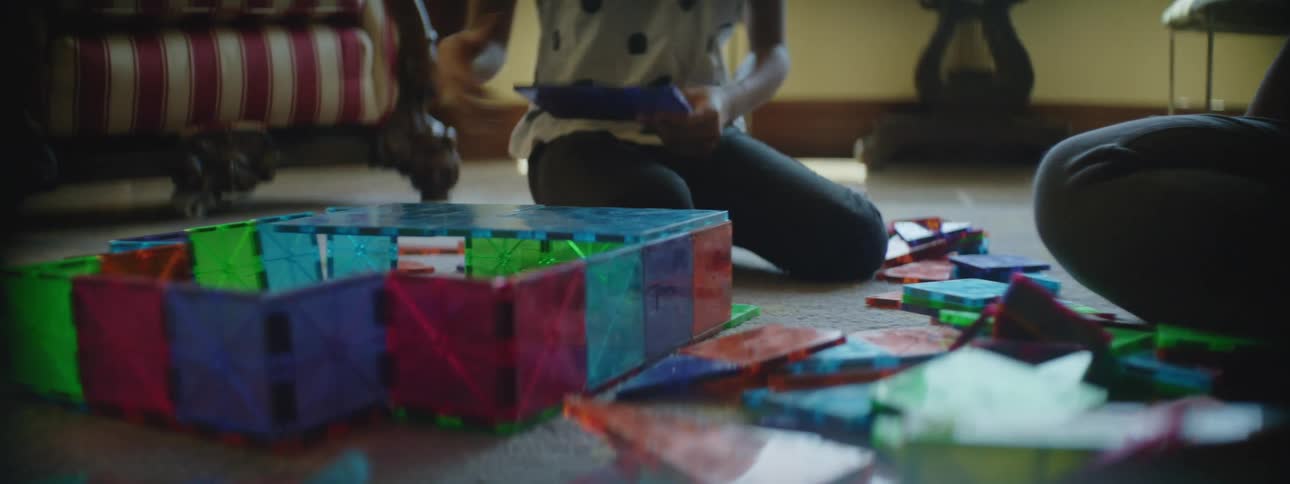 A mother and daughter sit on the floor together as they put colorful puzzle pieces together