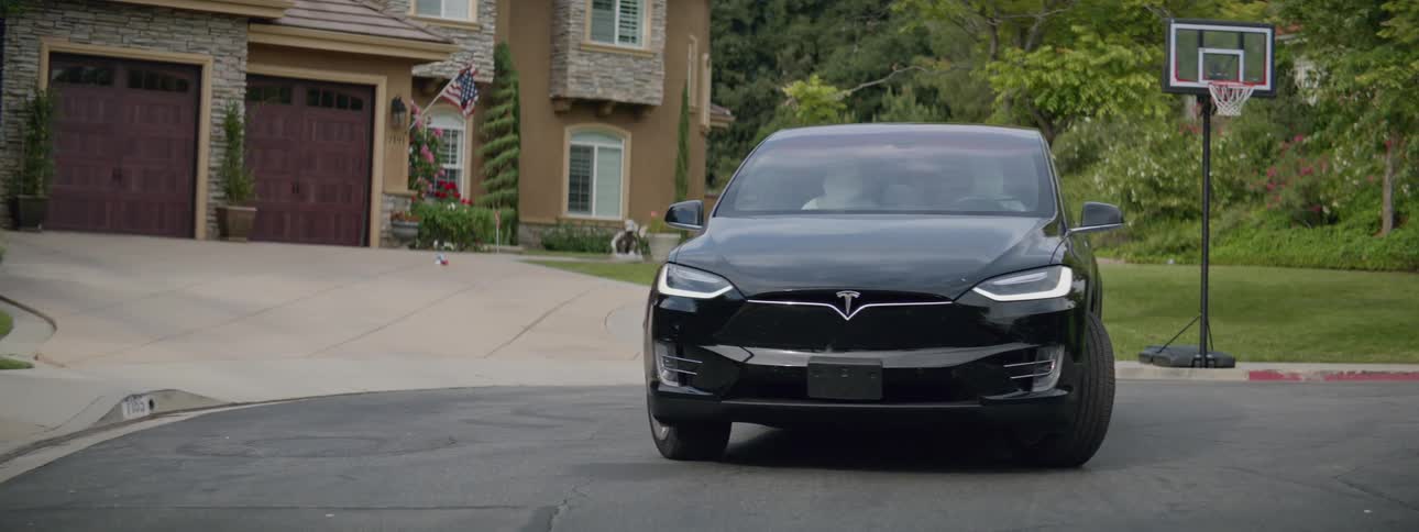 A black automobile is parked in front of a house near a basketball hoop