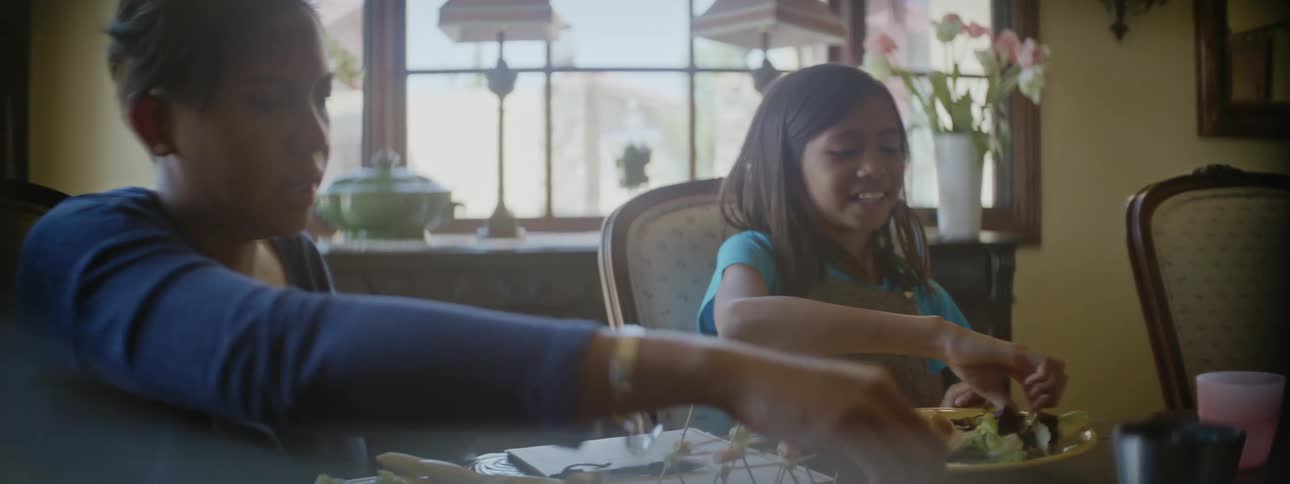 Grandmother and granddaughter sitting together at dining table eating and playing with toys