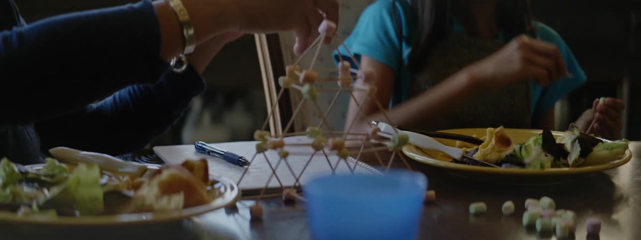 Woman and girl play marshmallow tower game sitting at table