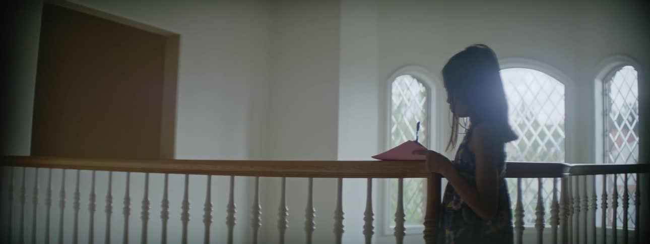 A young girl standing at a wooden railing while writing on a piece of paper