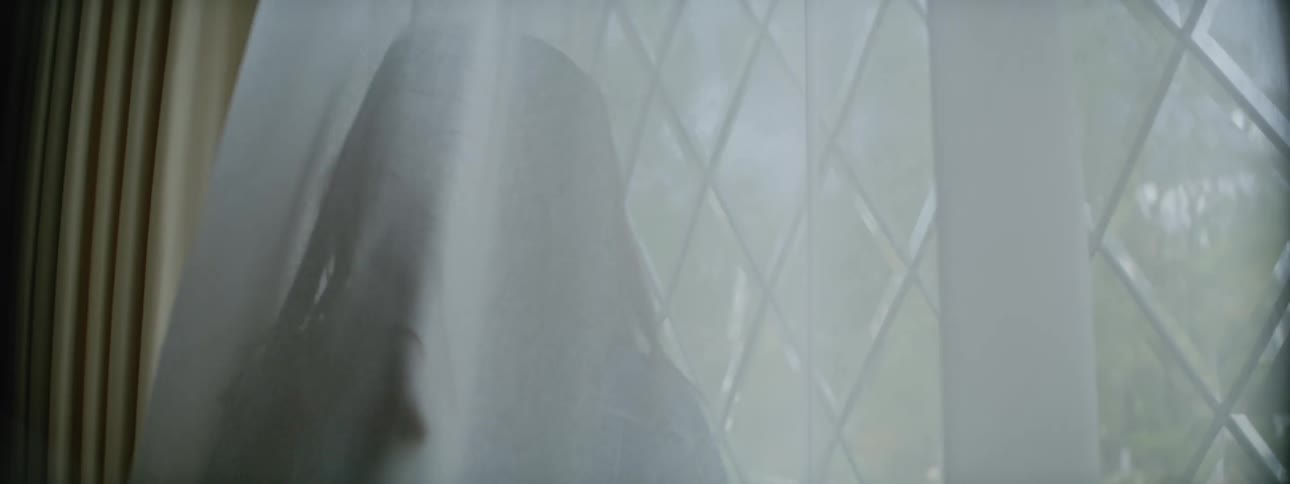 A young girl walking back and forth behind white curtains in front of a window