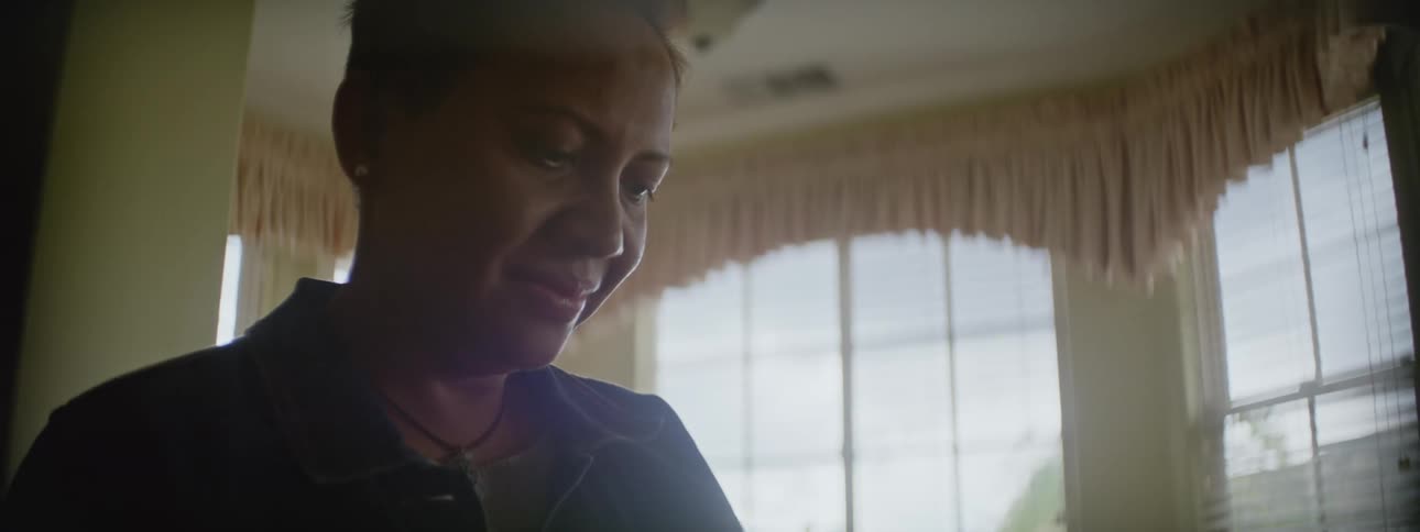 Woman with short hair and denim jacket looks down at thing and smiles slightly in the living room at home