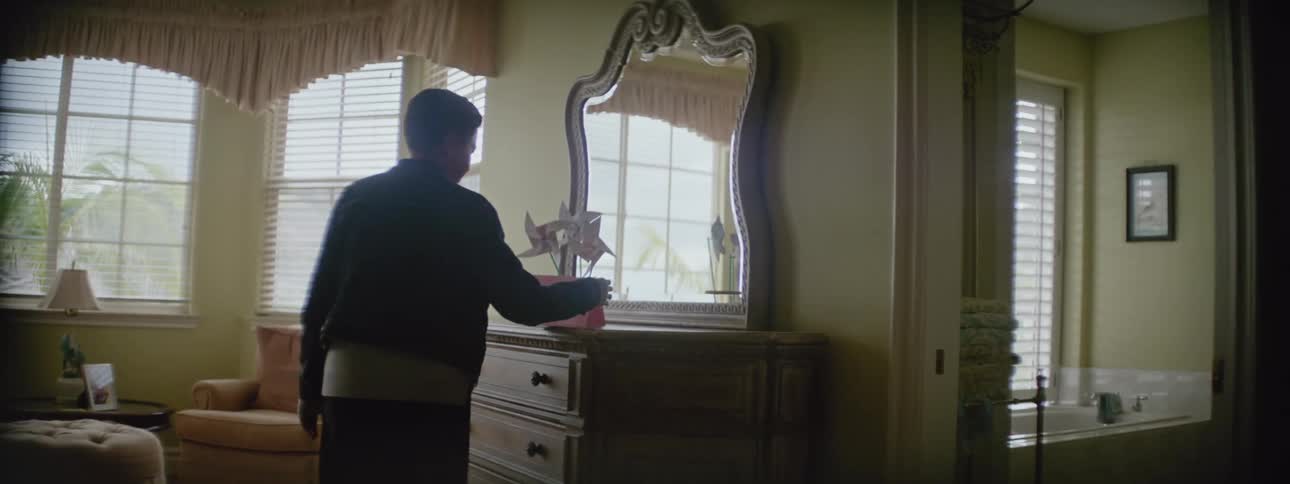A silhouette of a woman walking up stairs and into a bedroom picking up a card on the dresser and reading it