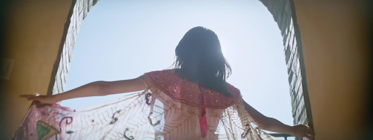 Girl opens her arms to extend a colorful translucent gauze cape in the balcony under the sun