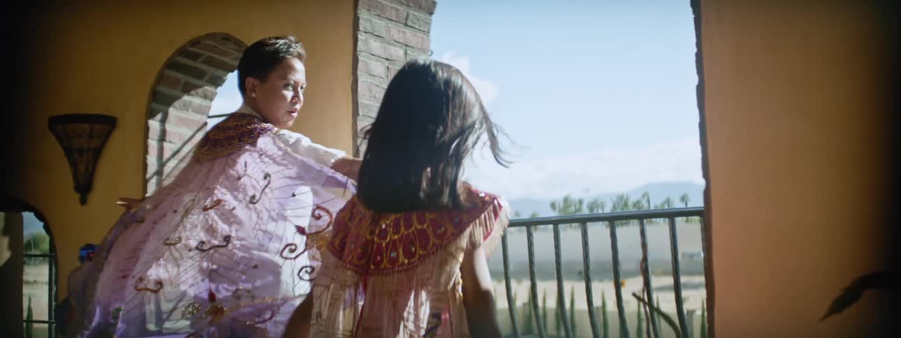 A girl and her mom wear matching dresses with sheer capes while standing in front of a window