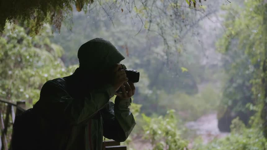 Silhouette of a photographer taking pictures close to a wooder railing near a river