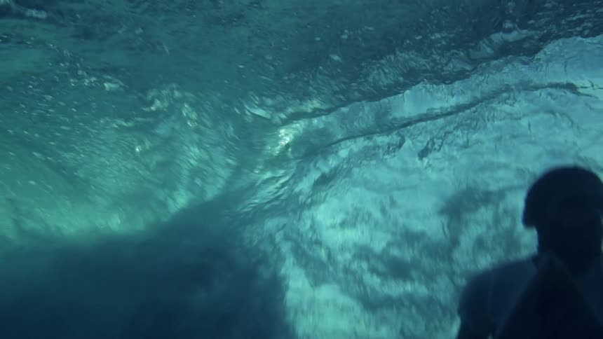Underwater footage of a young person over a surfboard floating under the sea waves