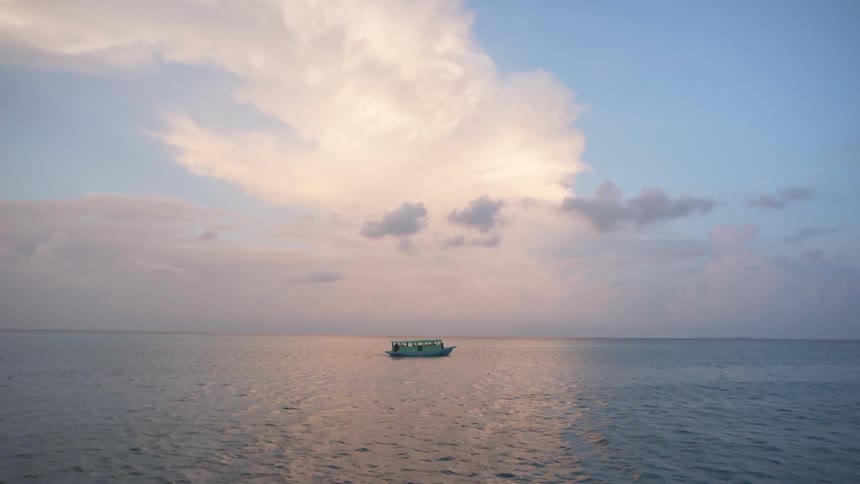 The sky and clouds reflect on the water as a boat is sailing on a beautiful day