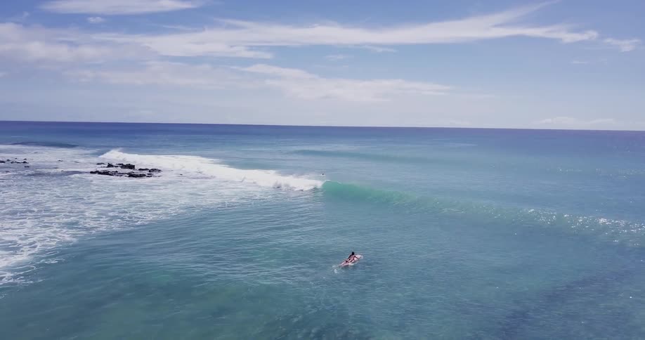 An aerial of the ocean as a person rides a wave and another person paddles out on a surfboard