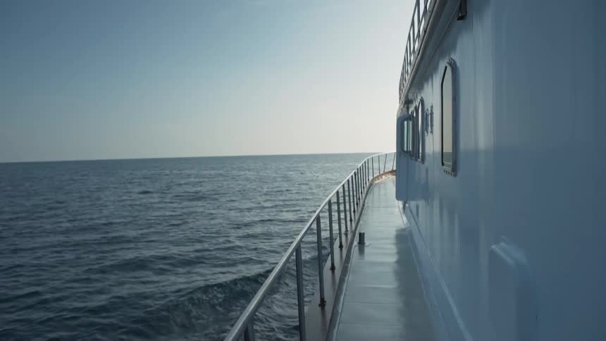 Ship with railed walkway cuts through ocean under a clear sky