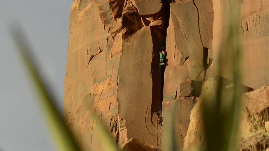 A woman rockclimbs up a steep desert cliff face on her own