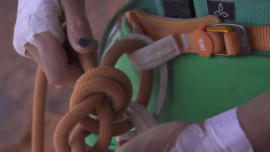 A close up of a person tying a rope around a harness around their waste