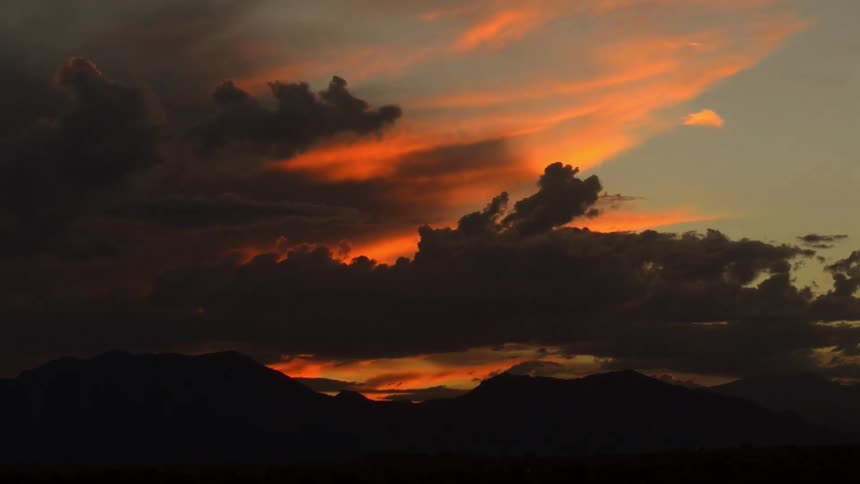 Time lapse footage of dark clouds with the sun orange afterglow behind them roll over the mountains