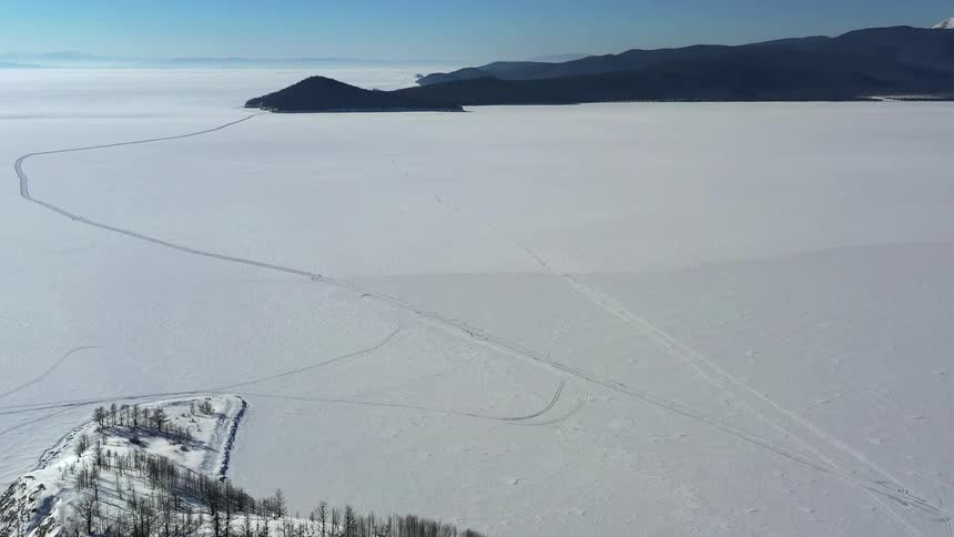 An aerial of snow covered lands with dark mountains in the distance