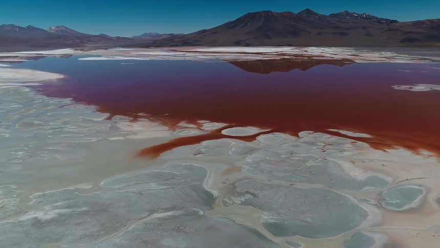 A body of water is completely brown from something and shows mountains behind it
