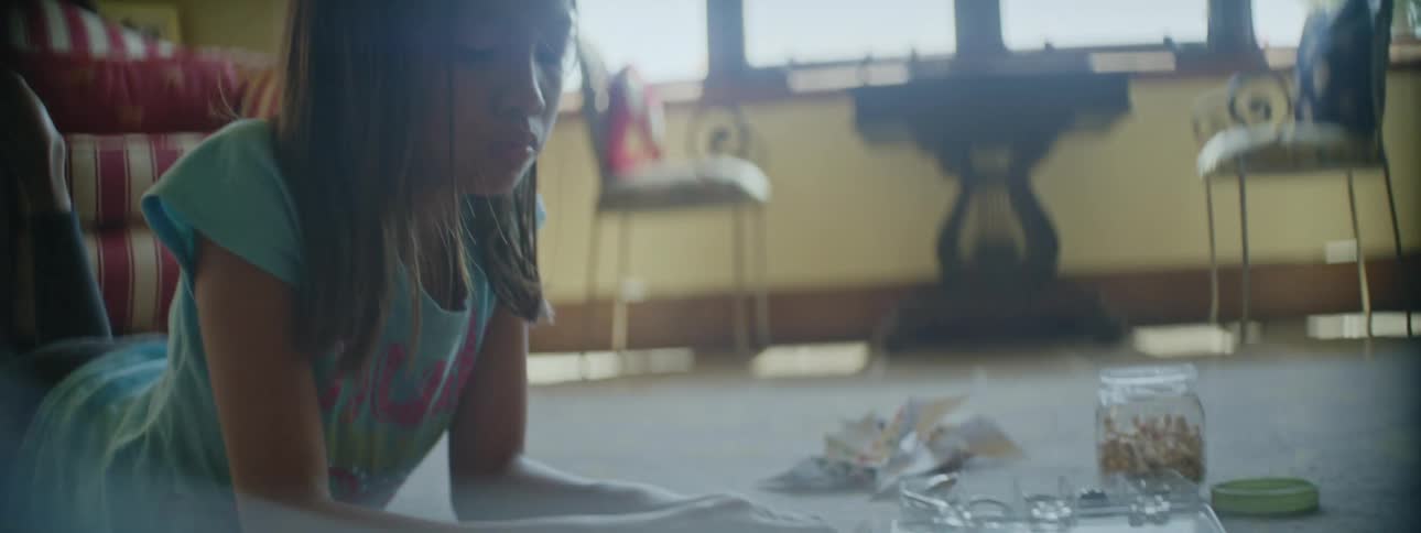 Girl laying over the carpet in the living room floor makes a paper windmill