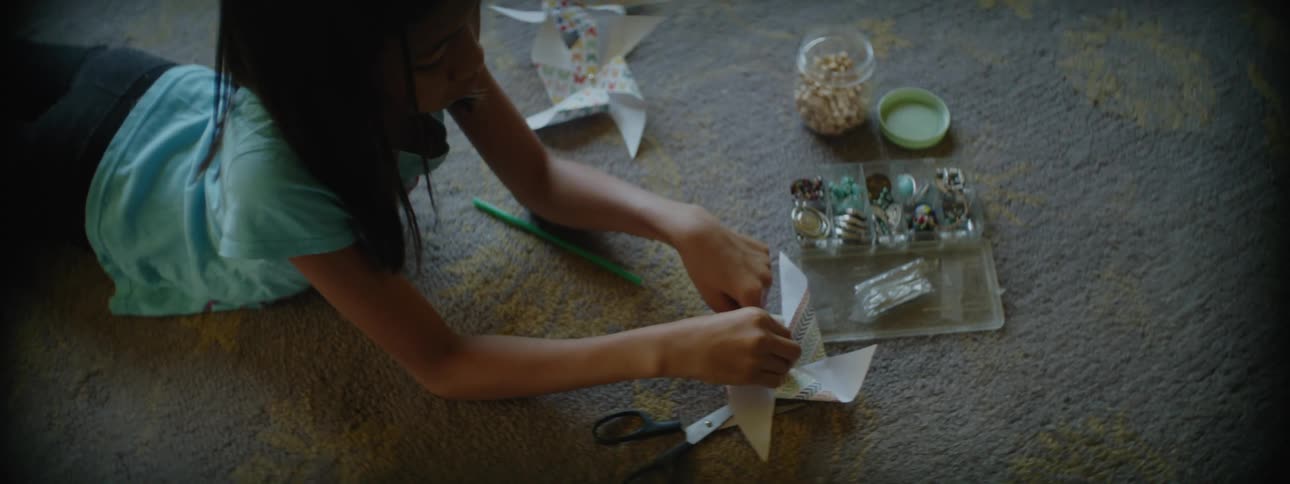Young girl on living room floor making pinwheels with beads and paper