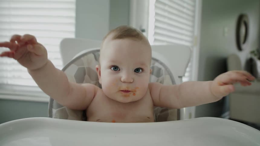 A young baby is getting fed food in a high chair