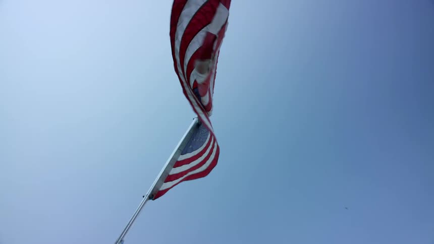 American flag waving in the wind in slow motion against a clear blue sky