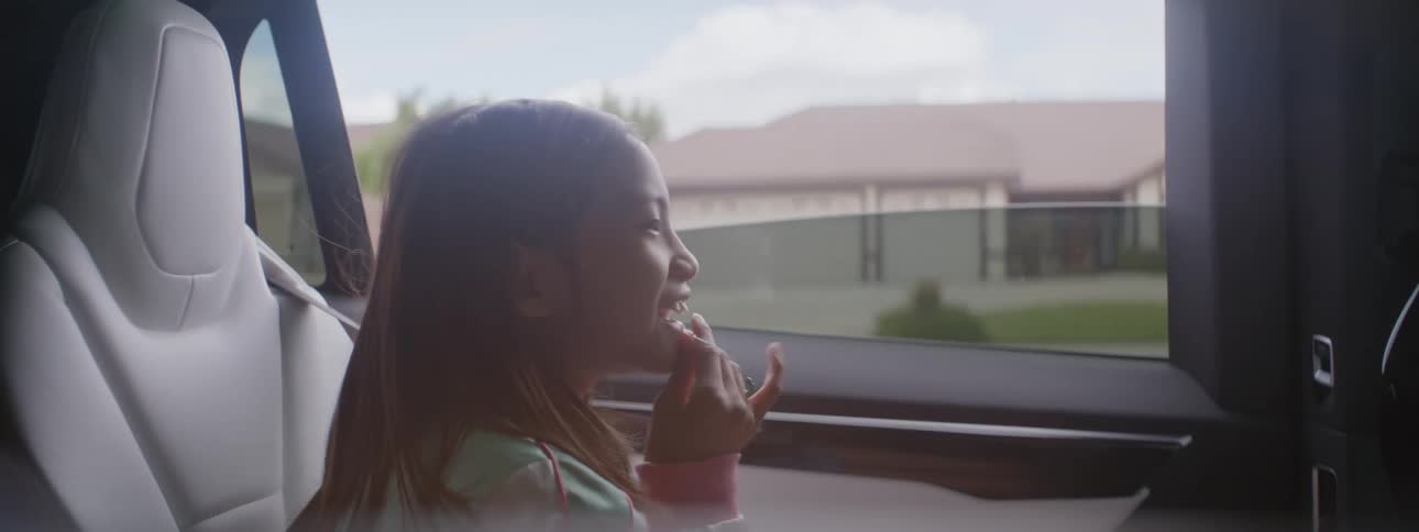 A woman is driving an automobile through a neighborhood and her little girl is sitting in the back seat