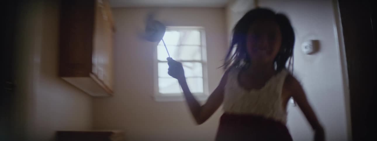 Happy young girl running around the house with a paper windmill