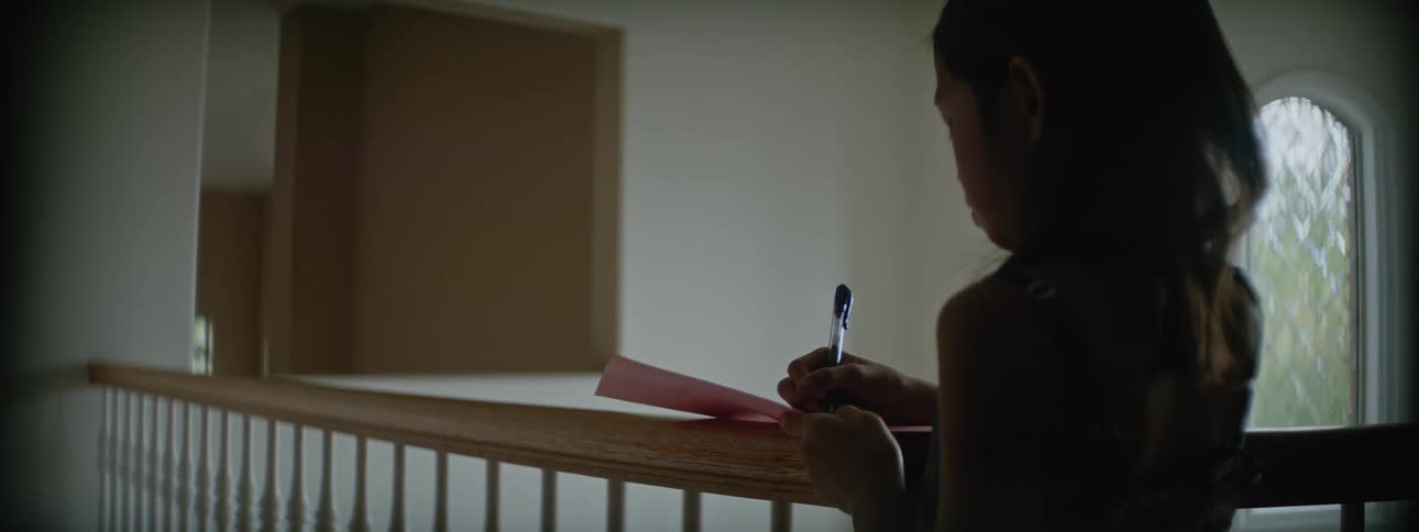 A young girl standing next to a railing writing on a piece of paper on it