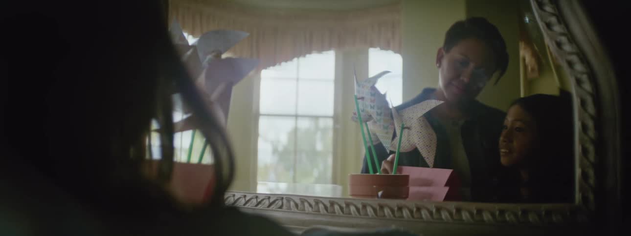 Mirror reflects mother and daughter as they examine pinwheels sitting in flowerpot