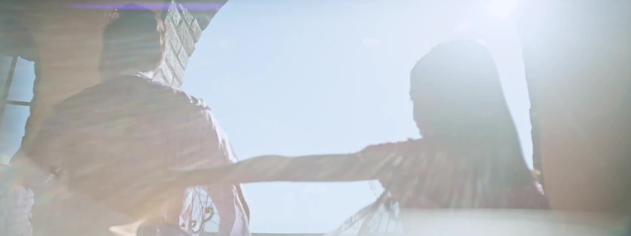 A mother and daughter standing in an open doorway as sun shines between them as they move their arms around