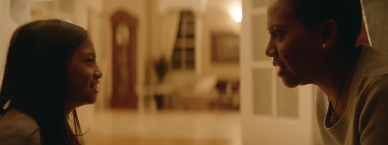 Woman with short hair earrings and necklace talks with girl smiling in the living room