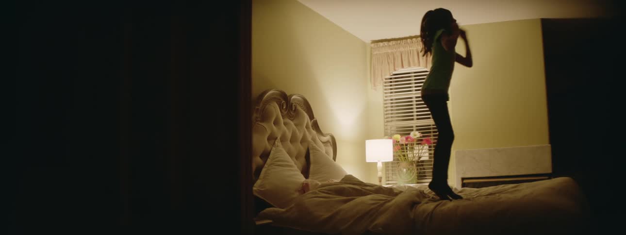 A girl jumps on a bed in a bedroom at night