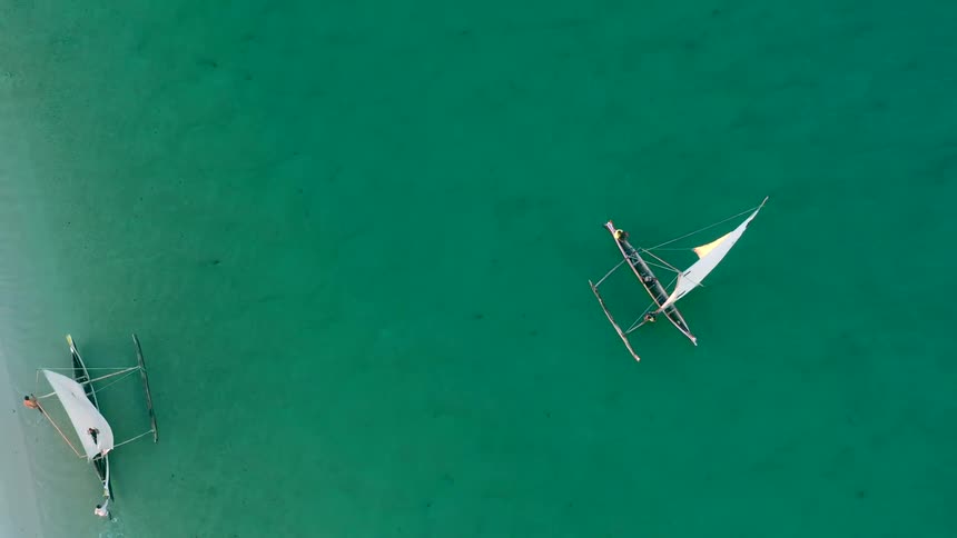Two outriggers sail past each other on green ocean