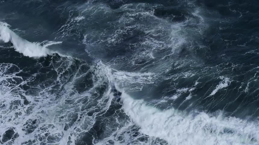 Looking down at rough water waves as they splash and roll in to shore