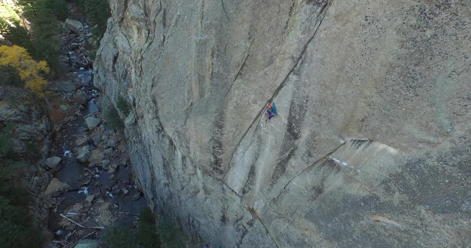 An aerial of a person on a rock face climbing the mountain
