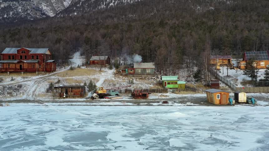 An aerial of an ice covered body of water with houses along the coast line against the hillside
