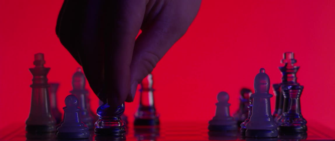 A closeup view of a hand moving a knight chess piece across a chessboard against a red background