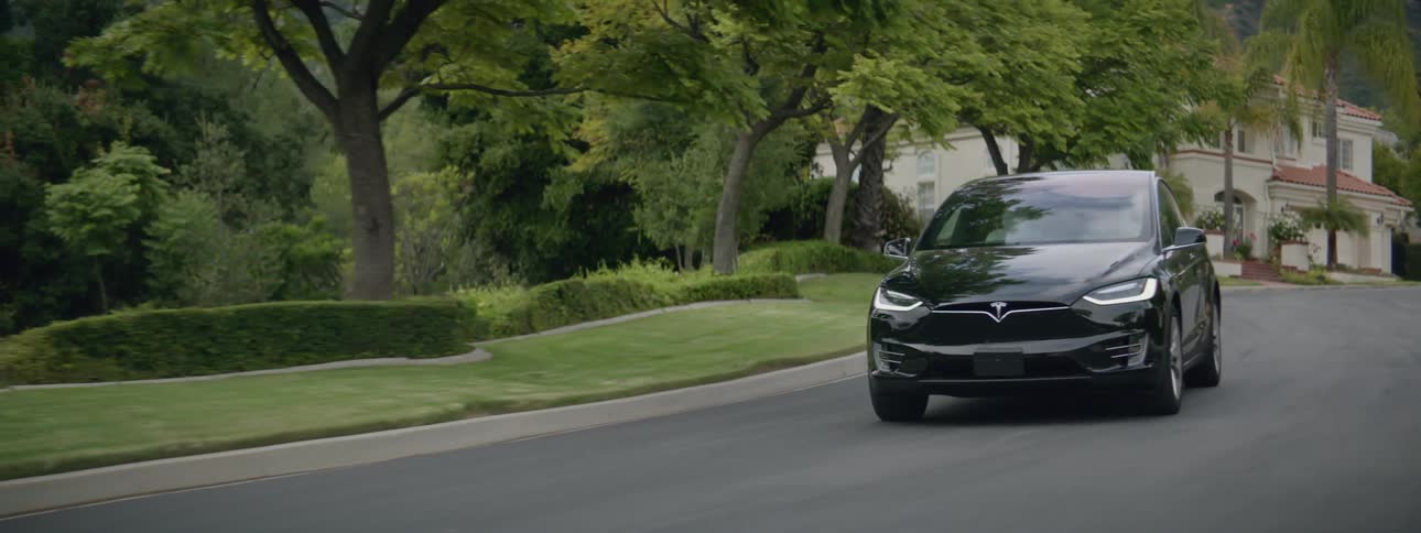 Black sedan drives along street away from mansion set among woods