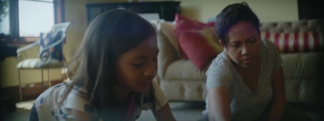A mother and her young daughter sit on the living room floor playing in front of the couch