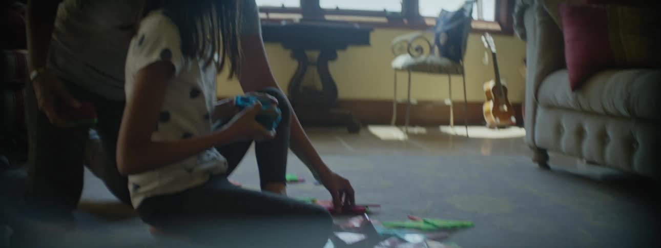 A young girl sitting on the floor picking up puzzle pieces as she hands them to her mother behind her