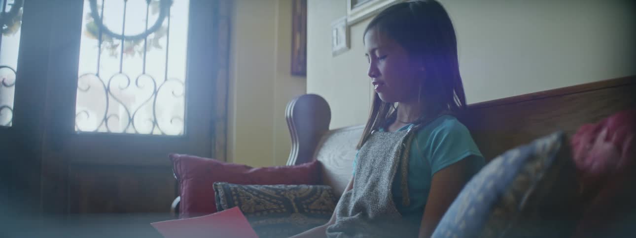 Young girl sitting on bench at home reading and writing on pink paper