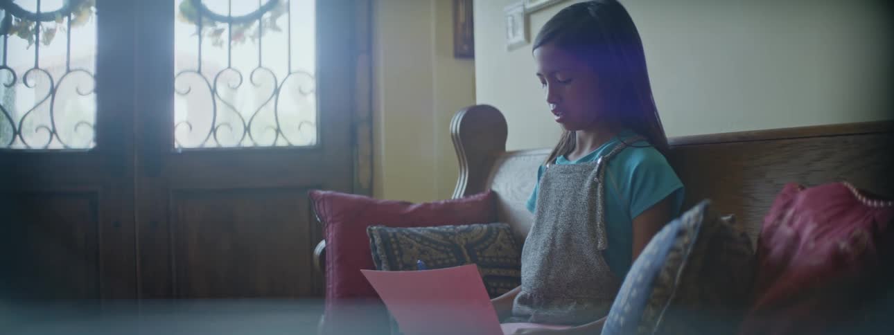 Young girl sitting on a bench in the foyer at home doing homework reading and writing
