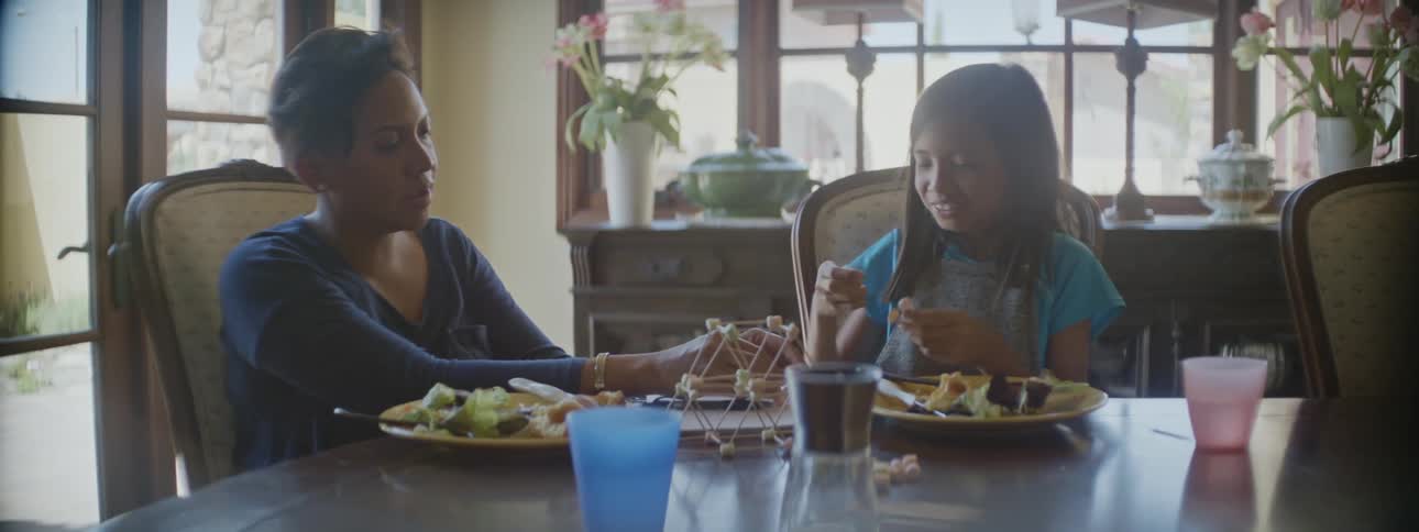 Mother and daughter are sitting at the table and eating food