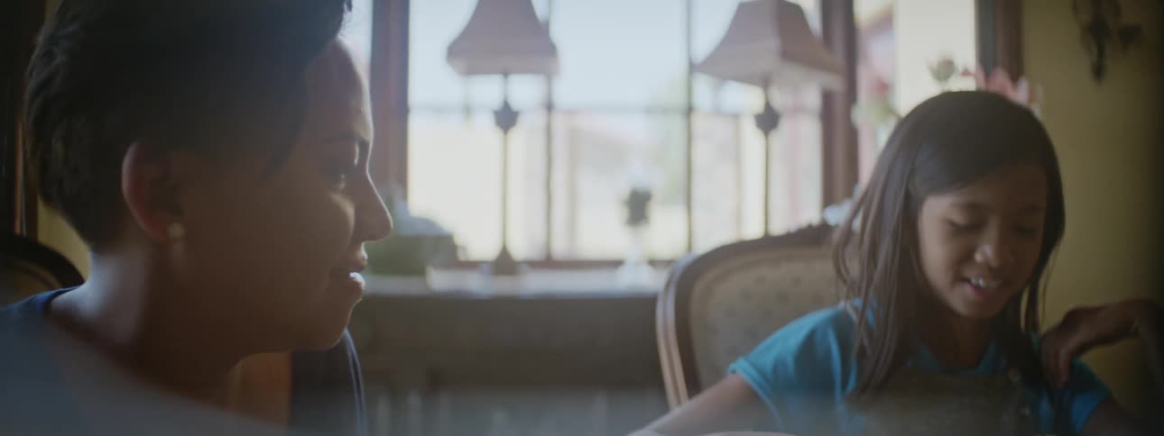 Mother and daughter laugh while eating at table with partly built construction toy