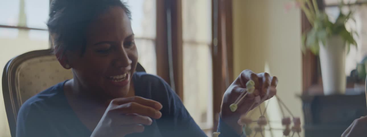 A mother and daughter sitting at a table playing with sticks laughing and smiling