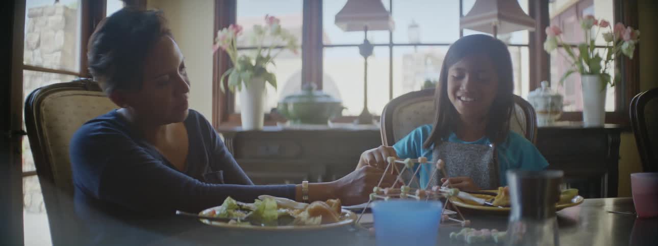 Mother and daughter share a meal at a table with model built from building toys