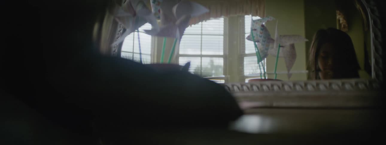 The backside of a young girl standing at a dresser writing something as her reflection is shown in the mirror