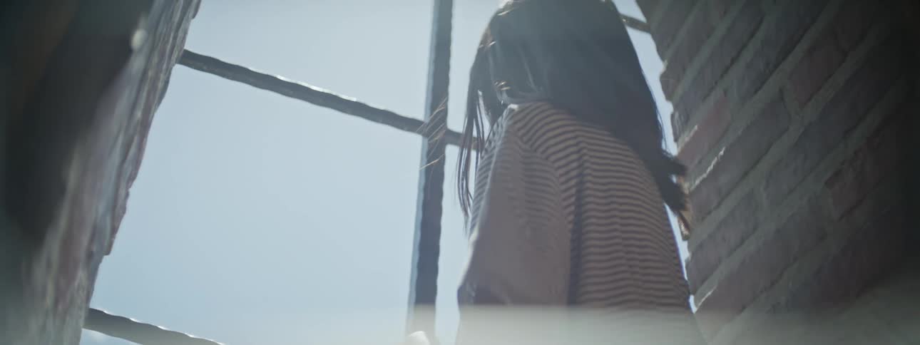 A girl holds onto a broken window frame while looking outside