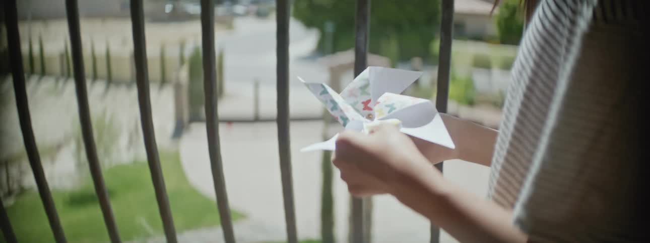 An up close of a young child in front of a railing holding a paper pin wheel in their hands