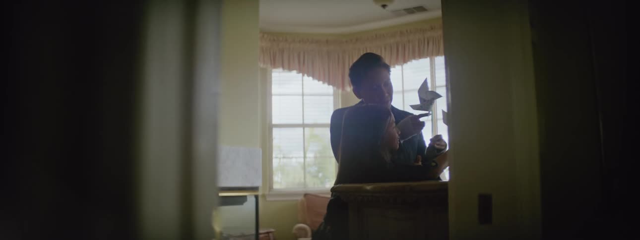 A woman shows a little girl a pinwheel inside a room in a house