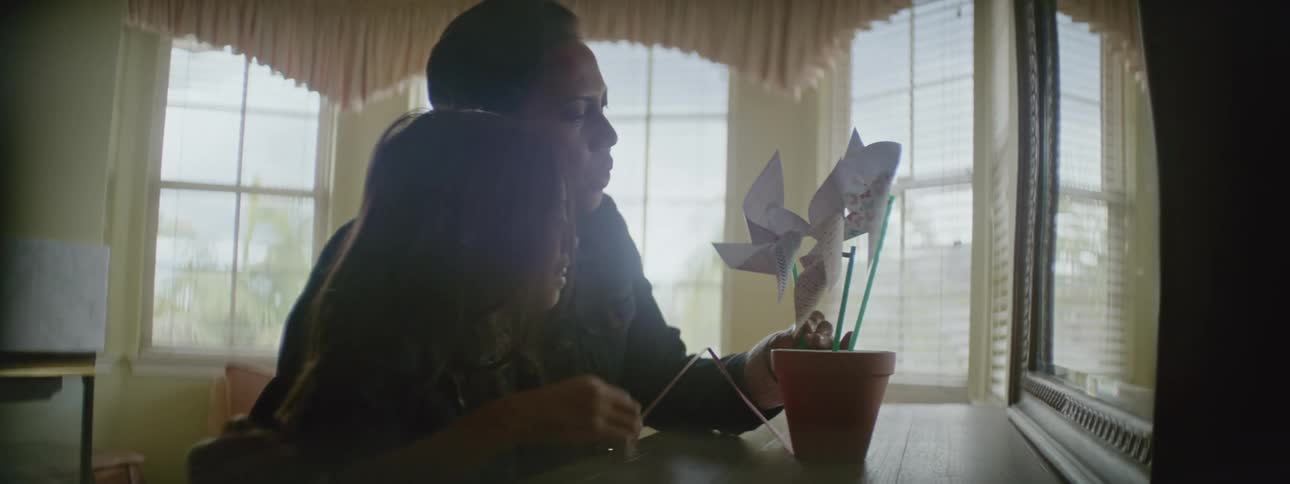 A woman and a little girl stand at adresser blowing paper spin wheels